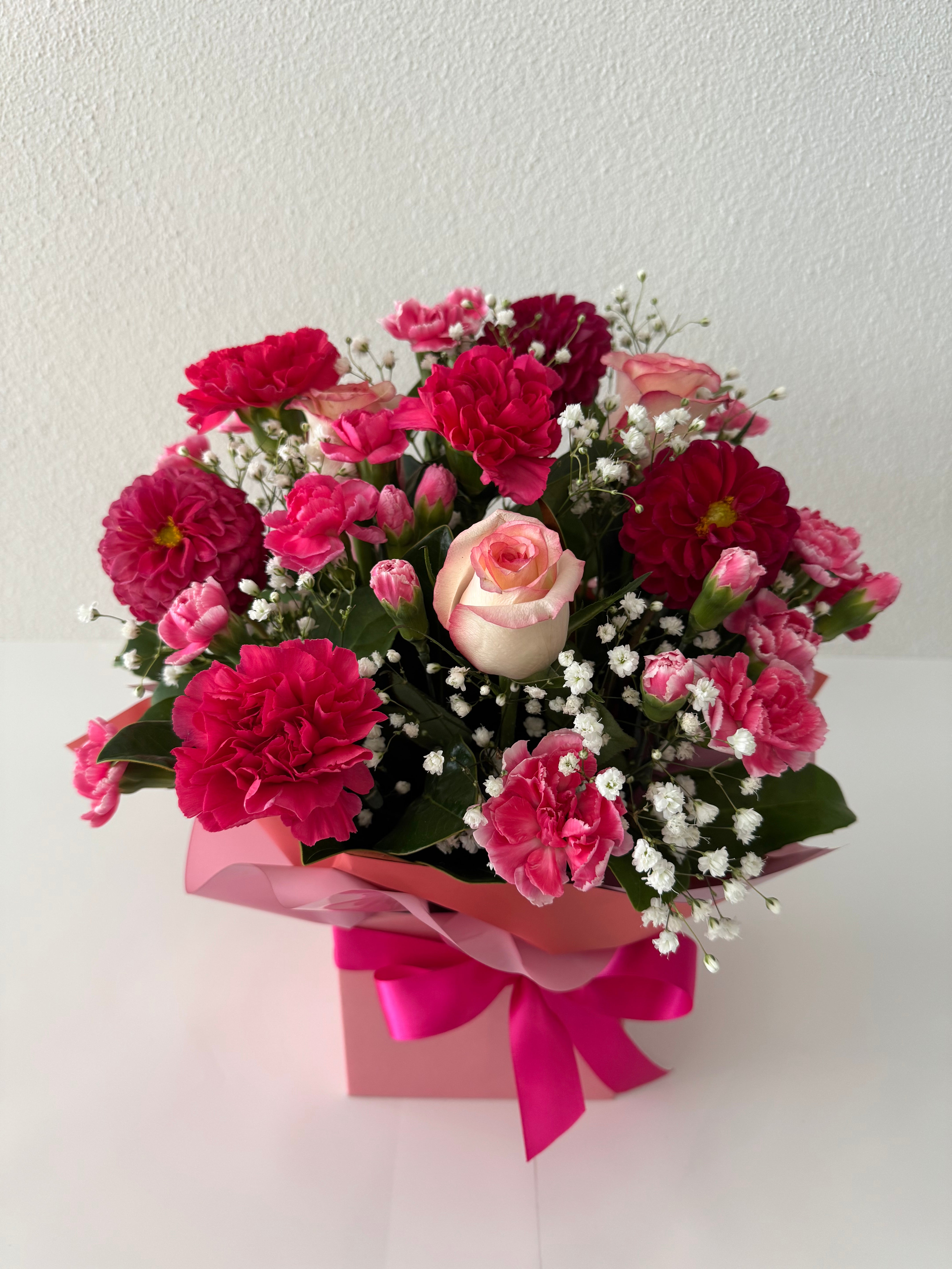Seasonal boxed blooms-A boxed floral arrangement featuring dahlias, mini carnations, mini roses, and gerberas with filler in a mix of pink, red, and white colors