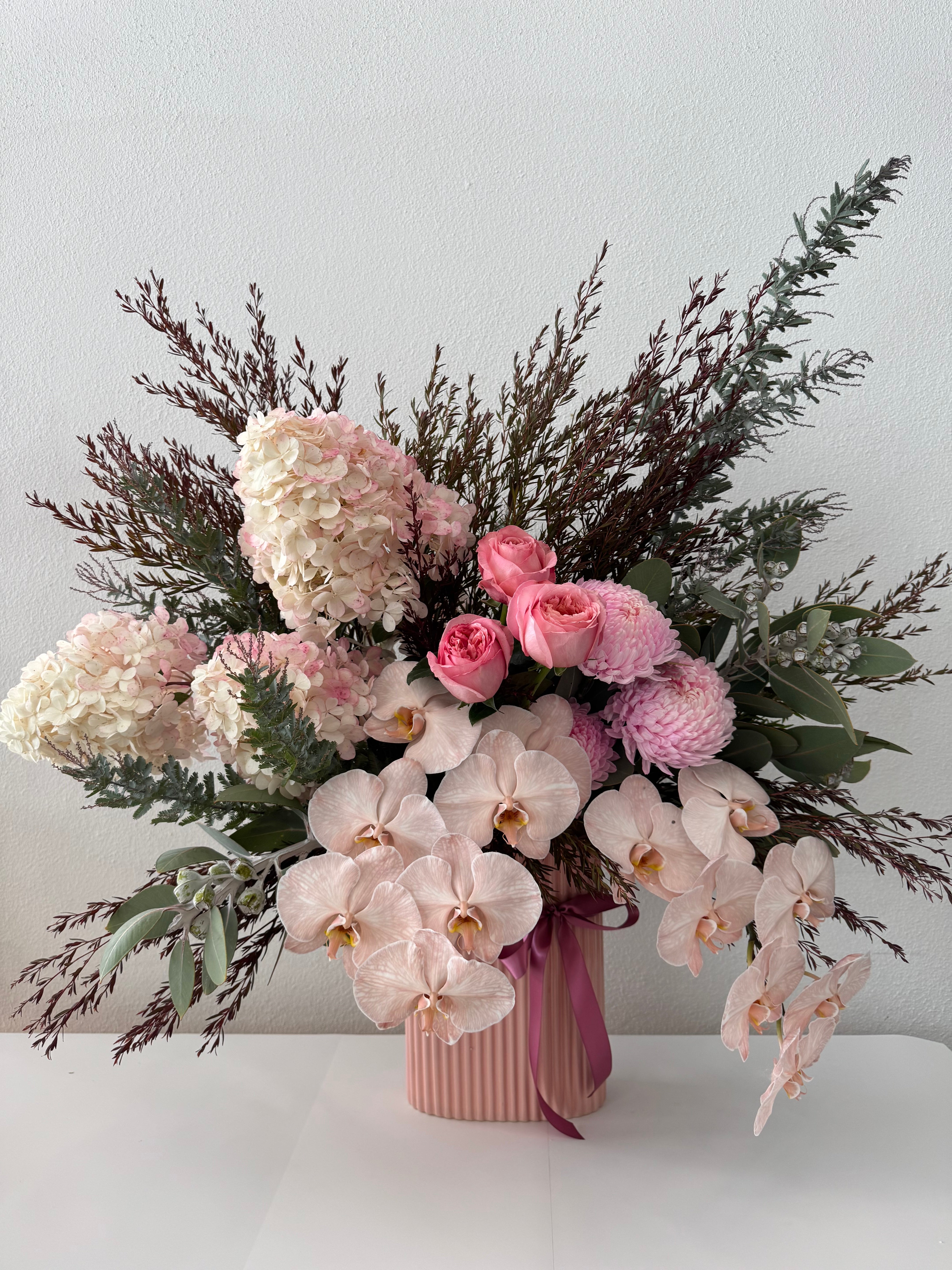 A floral arrangement featuring pink roses, blush blooms, and orchids with lush green foliage