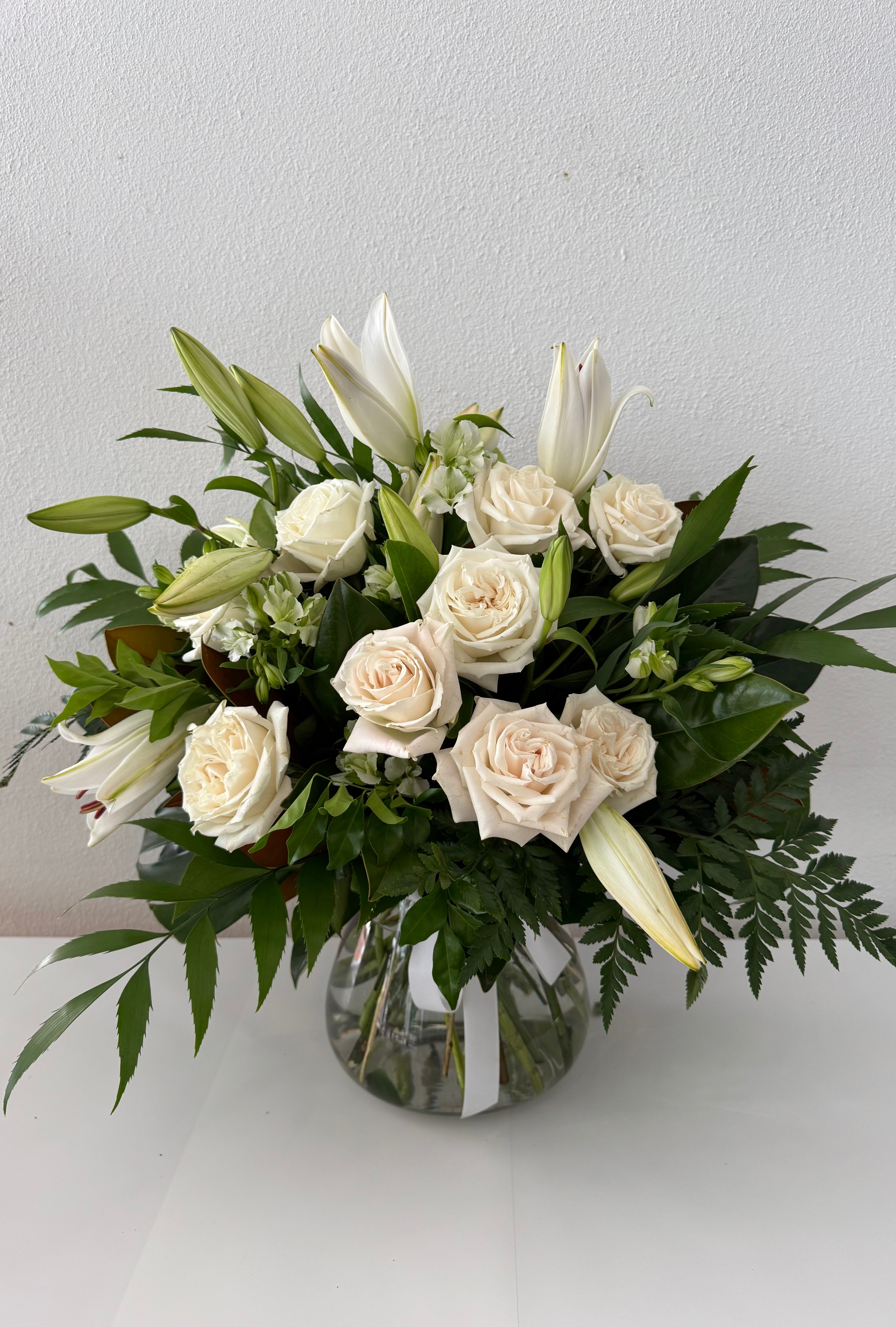 A medium-sized bouquet of all white flowers, featuring roses and lilies, arranged