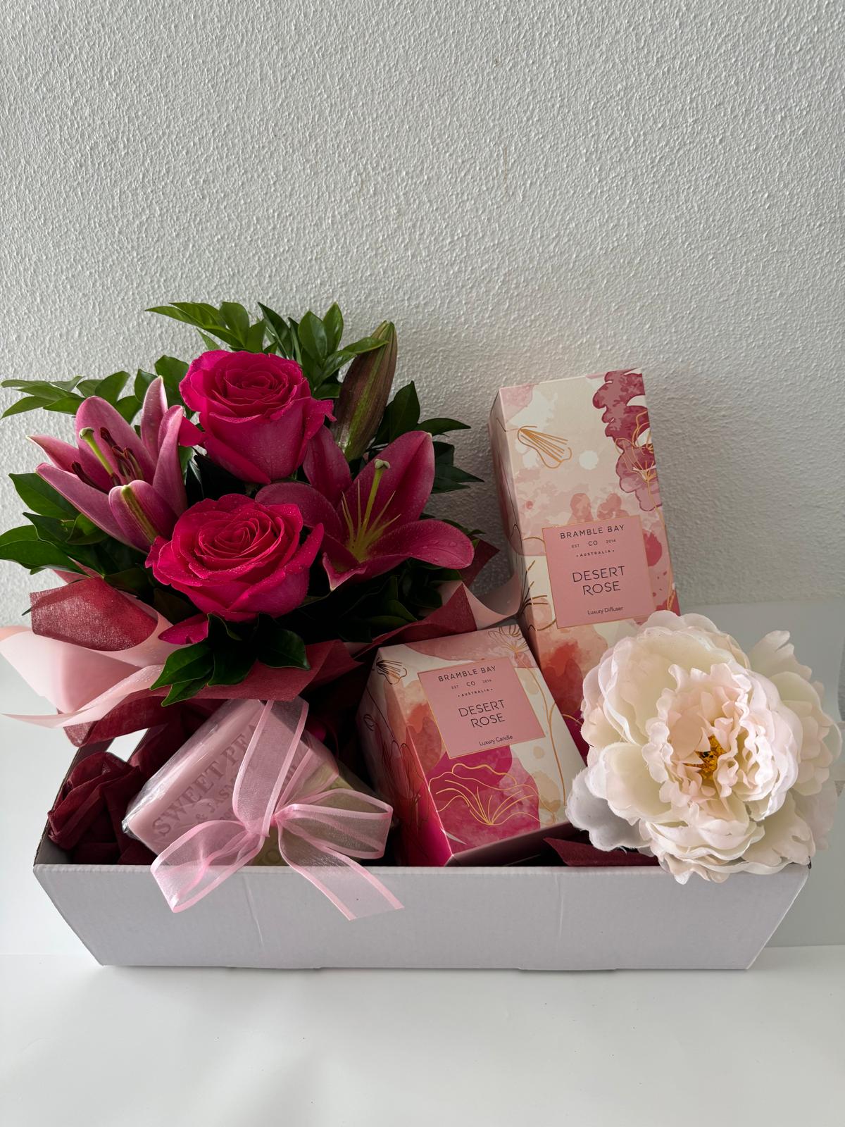 A gift basket containing an assortment of pink and white flowers, a candle, diffuser, and soap,