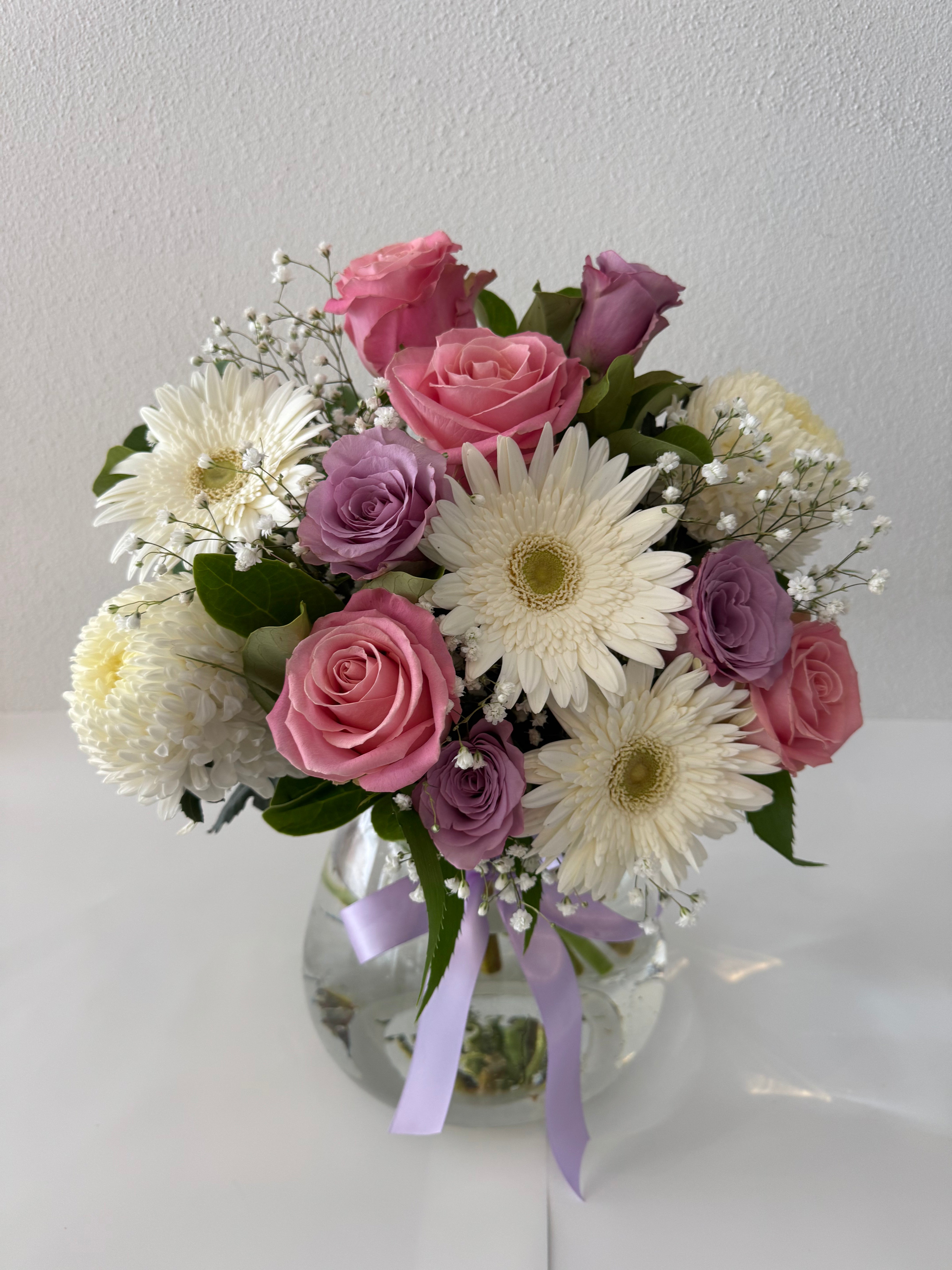 Pastel mixed blooms-A glass vase containing an arrangement of pink and white blooms, including roses and daisies