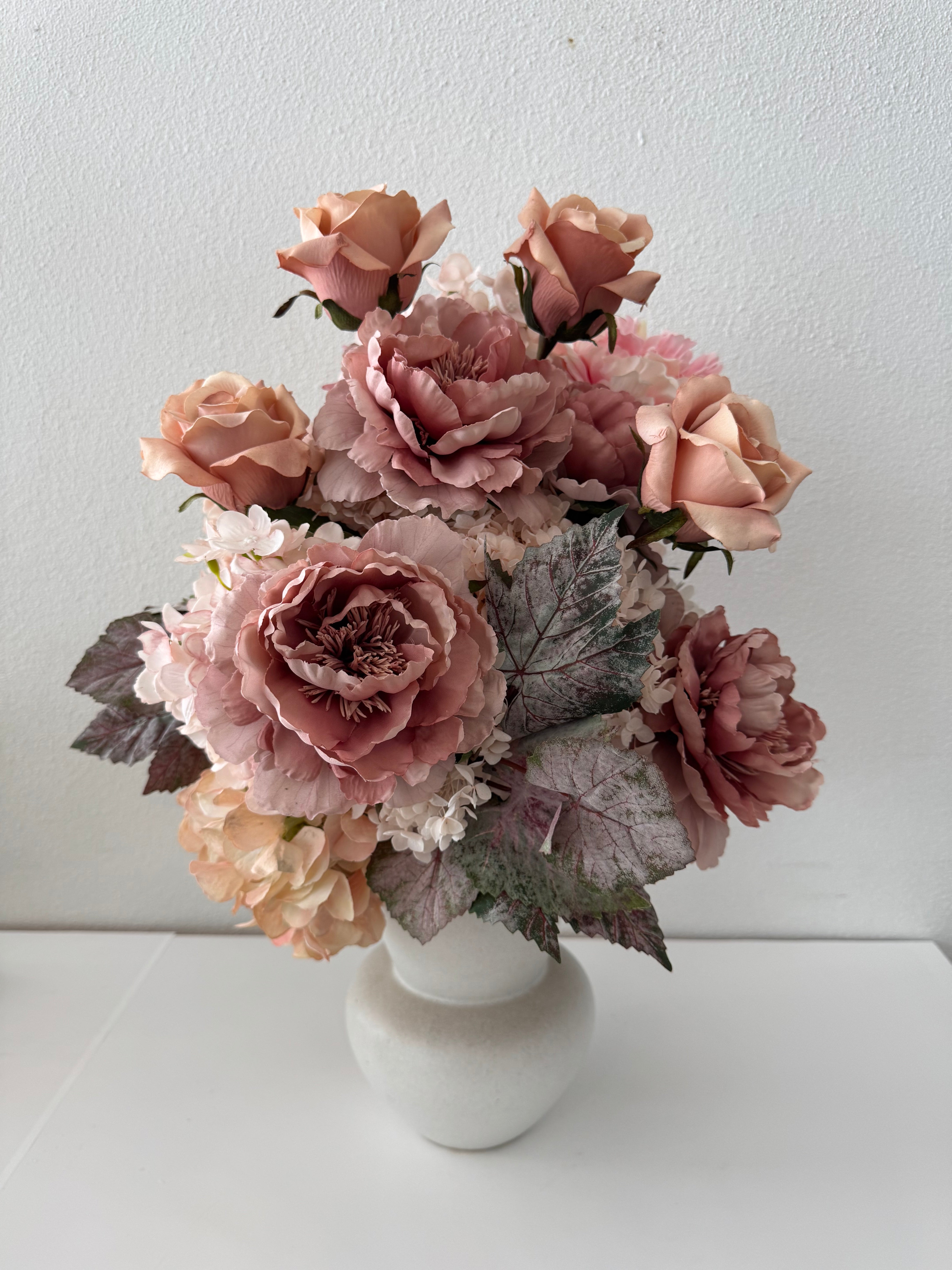 A bouquet of artificial flowers in autumn tones, with pink, brown, and white colors, arranged in a white ceramic pot