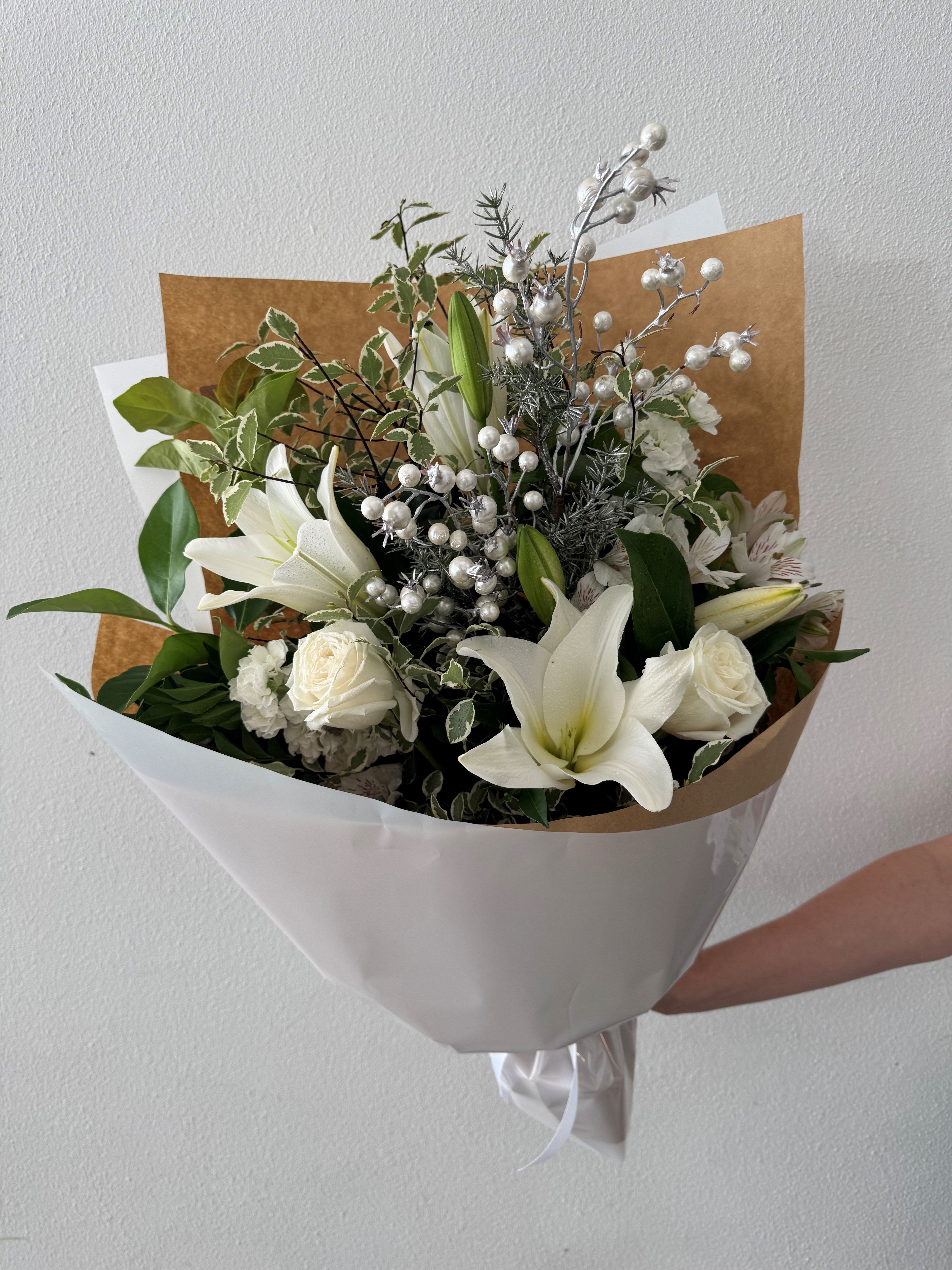A bouquet of flowers including white lilies, greenery, and bead-like flowers