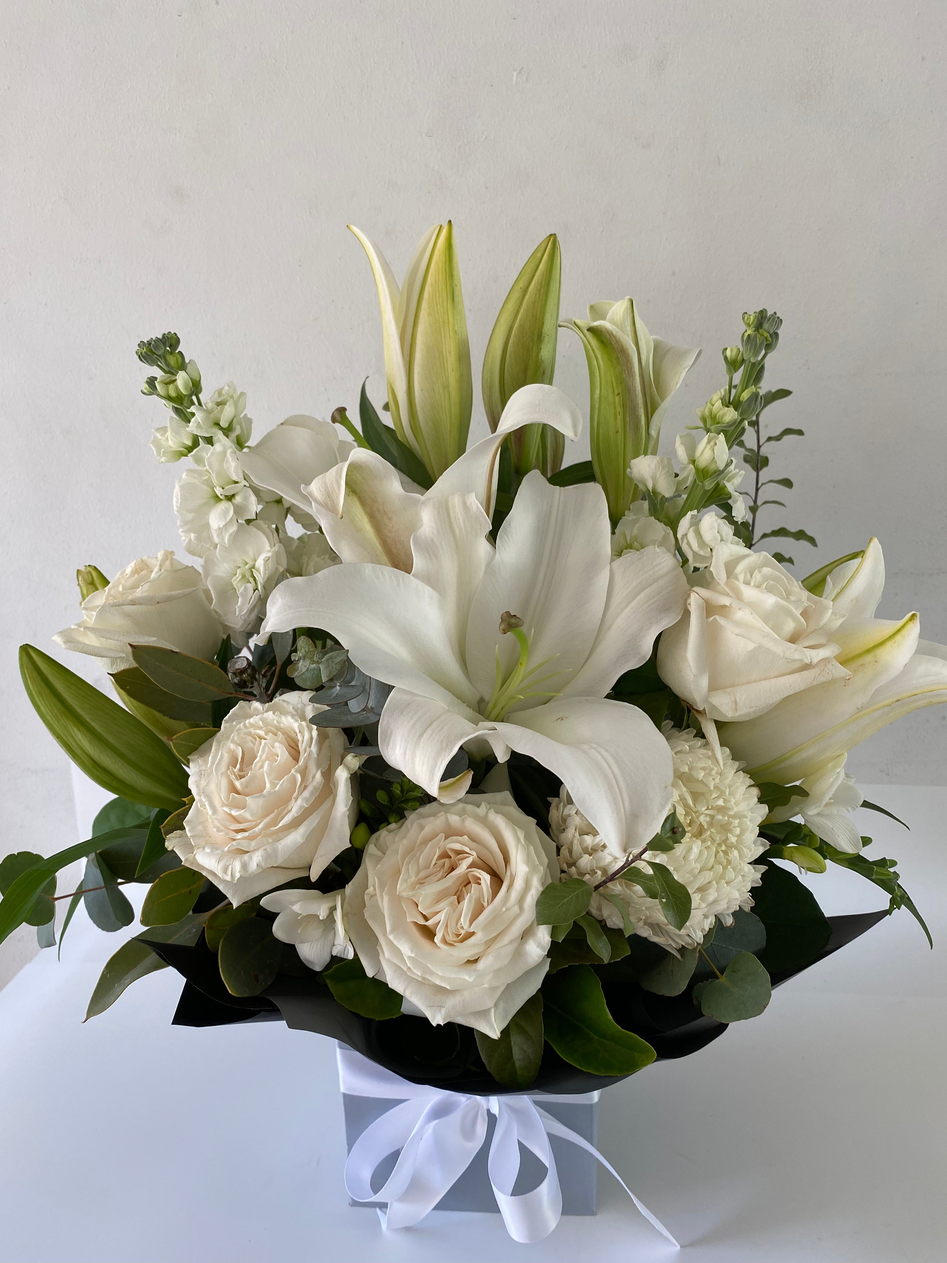A medium sized floral arrangement featuring white oriental lilies, roses, and other seasonal flowers