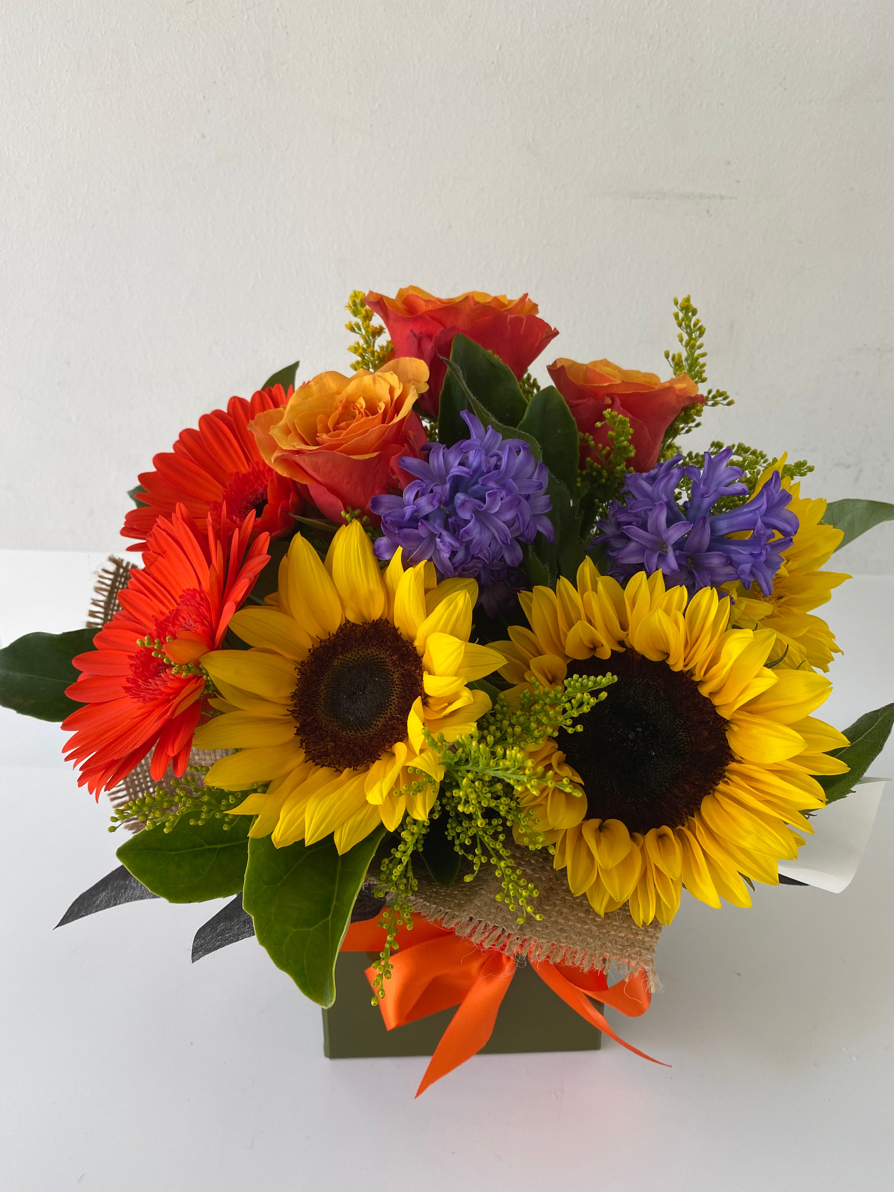 A floral arrangement featuring sunflowers and other flowers in shades of orange, red, and purple
