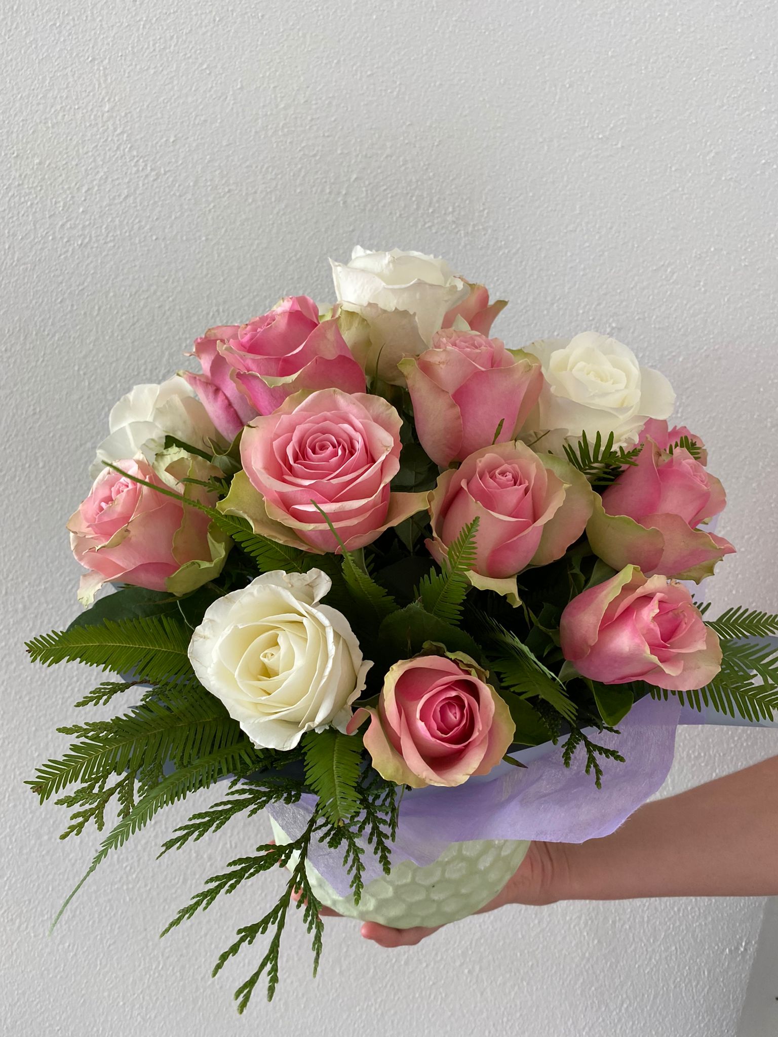 A bouquet of pastel pink and white roses held in a ceramic pot